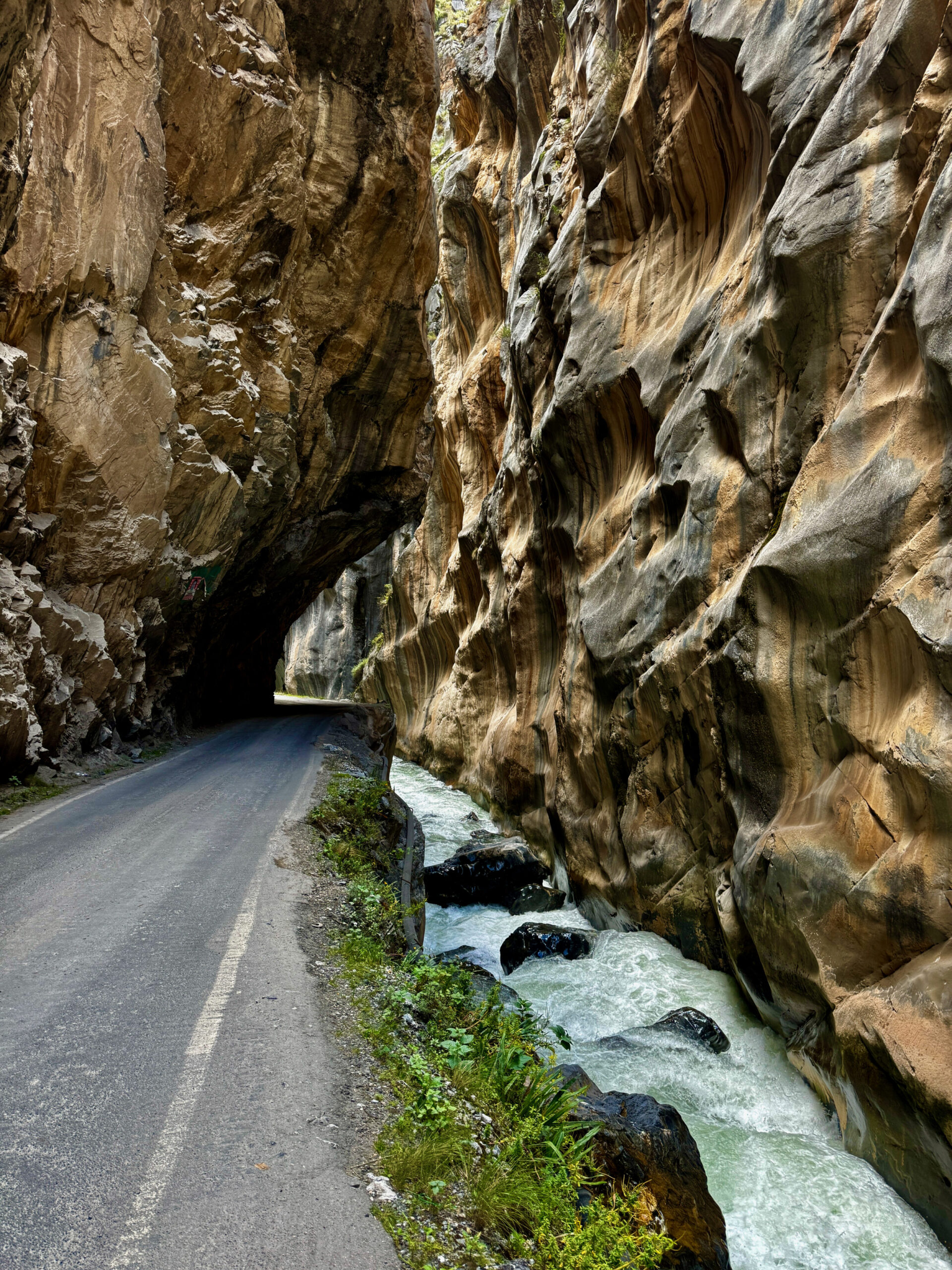Estrada estreita entrando em tunel escavado na rocha, com rio ao lado, nos Andes peruanos