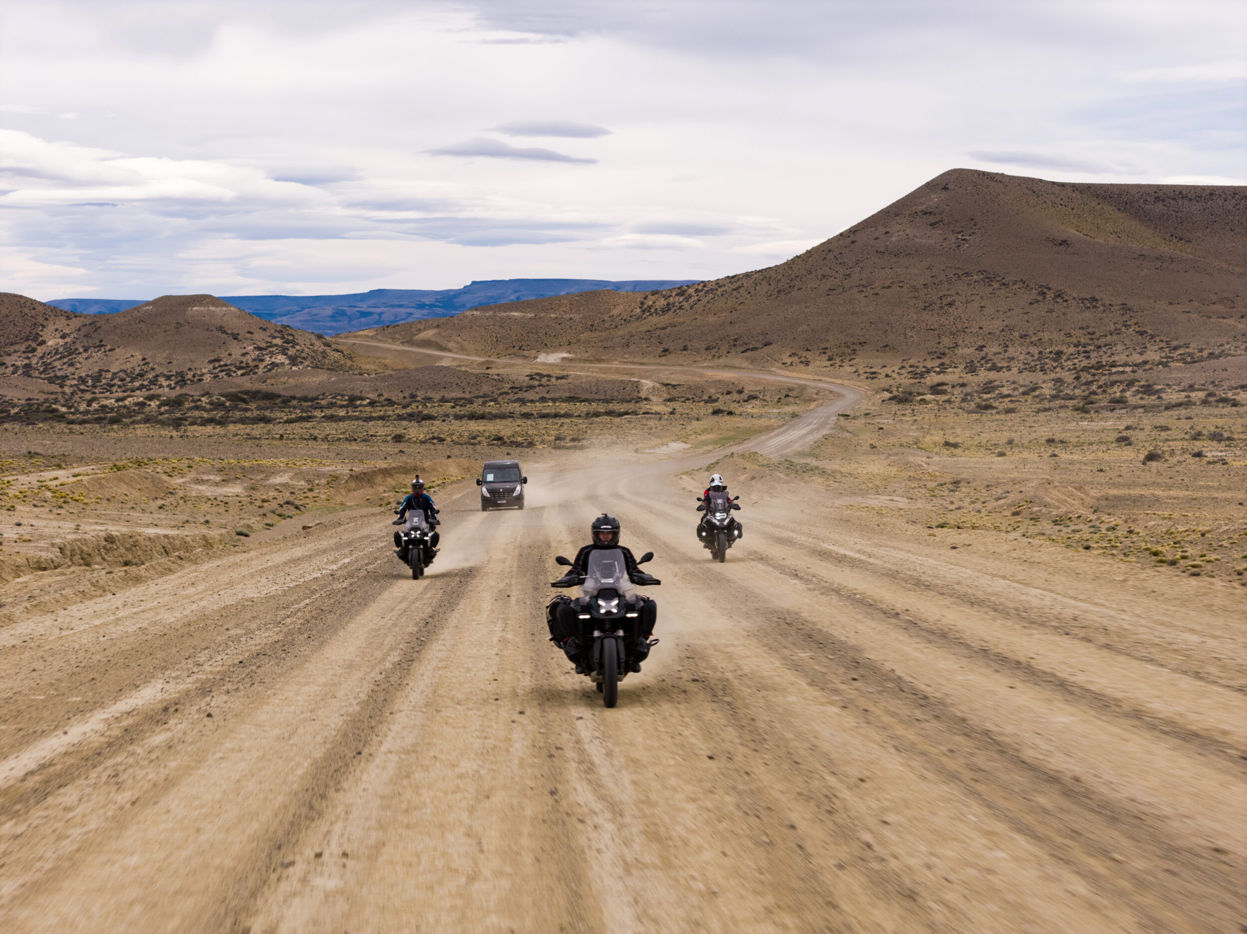 Caravana de motos BMW UpSerra em estrada de ripio na estepe patagônica com poeira levantando