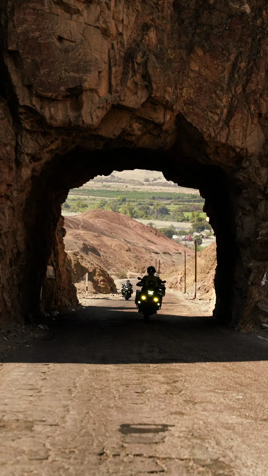 Moto saindo de um túnel de pedra para o vale, na estrada