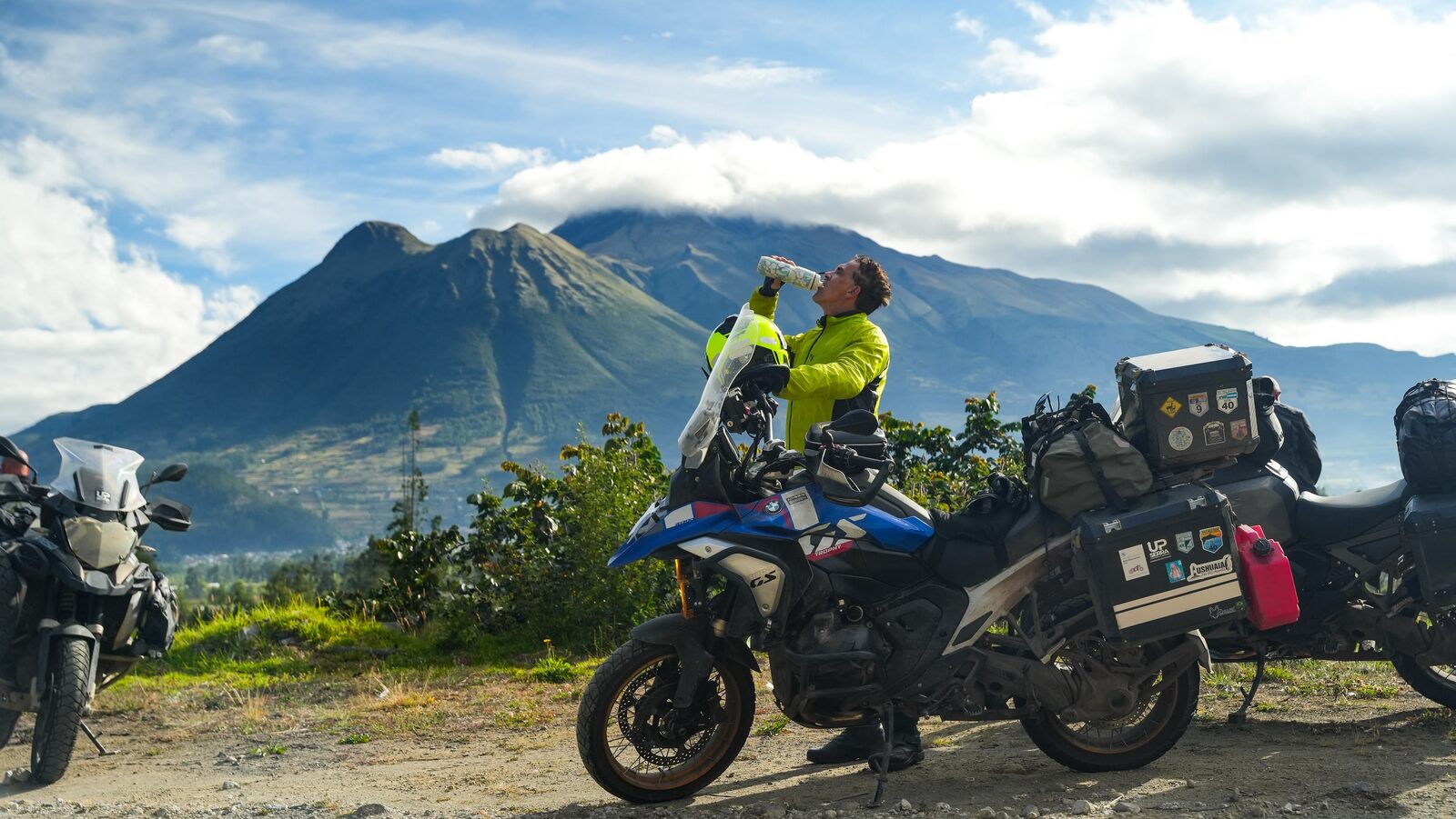 Piloto e moto diante de um vulcão com nuvens no cume, no norte do Equador rumo a Otavalo.