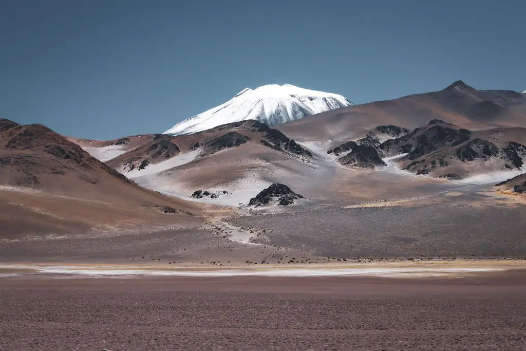Vulcao nevado ao fundo de um vale seco no deserto do Atacama