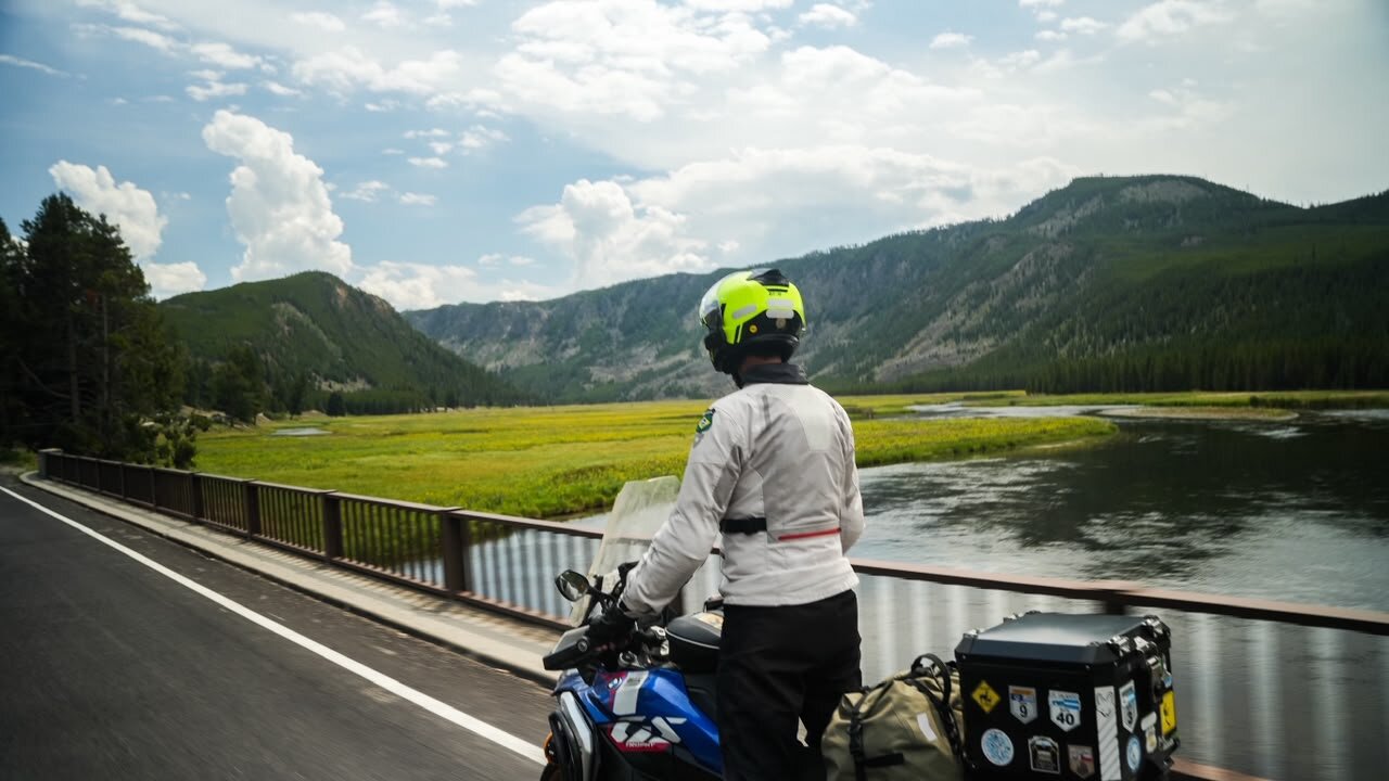 Piloto parado sobre a moto contemplando um vale com rio em Yellowstone